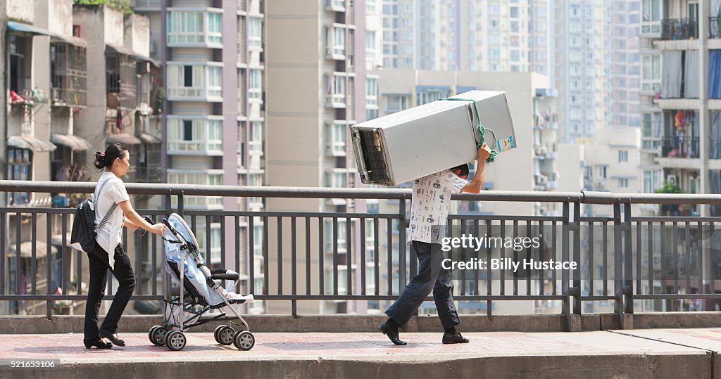 A family walking together, with the father carrying a large appliance on his back in an Asian city