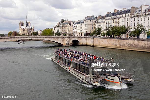 a tourist boat floats past ile. st. louis with notre dame cathedral in the background - seine maritime stock pictures, royalty-free photos & images