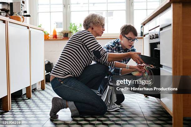 mature mother teaching her teenage son how to bake - adult helping teenager stock-fotos und bilder