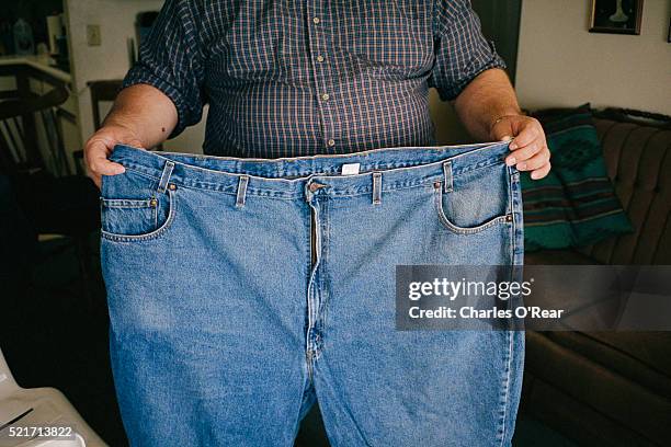 overweight man holding jeans - adelgazar fotografías e imágenes de stock