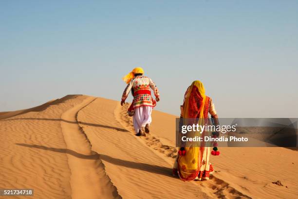 man and woman walking on sand dune, jaisalmer, rajasthan, india, asia - jaisalmer stock-fotos und bilder