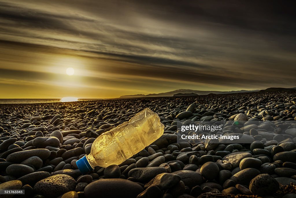 Water bottle on a rocky beach at sunset.