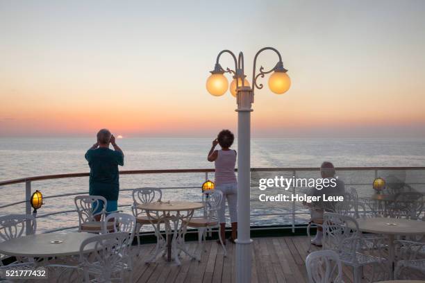 passengers enjoy and photograph the sunset from aft deck of cruise ship ms deutschland (reederei pet - ms deutschland cruise ship stock-fotos und bilder