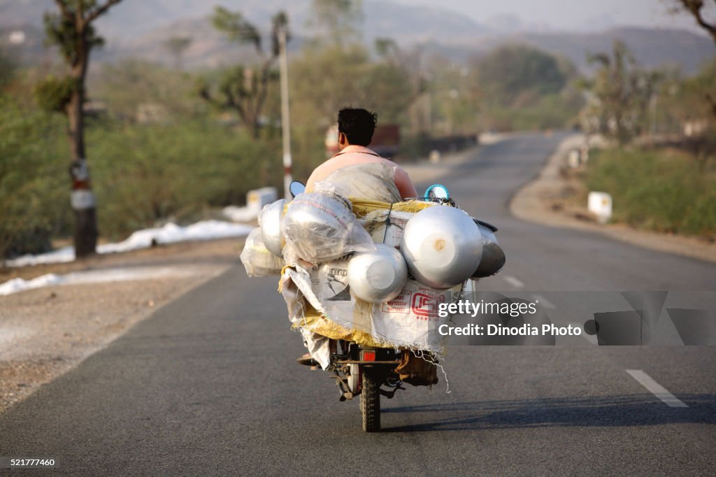Milkman riding on two wheeler carrying milk cans, India