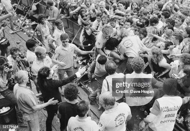 Singer Bono watching medical staff remove a fan from the front of the Live Aid crowd at Wembley, 13th July 1985.