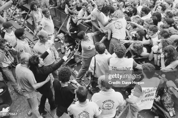 Singer Bono watching medical staff remove a fan from the front of the Live Aid crowd at Wembley, 13th July 1985.