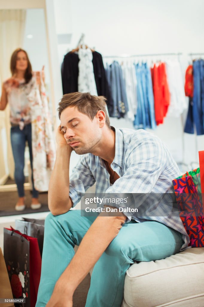 Homem entediado fazendo compras com namorada em loja de roupas