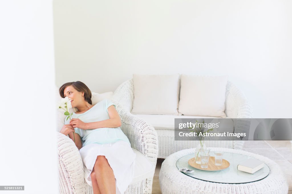 Woman smelling flowers in wicker chair in living room