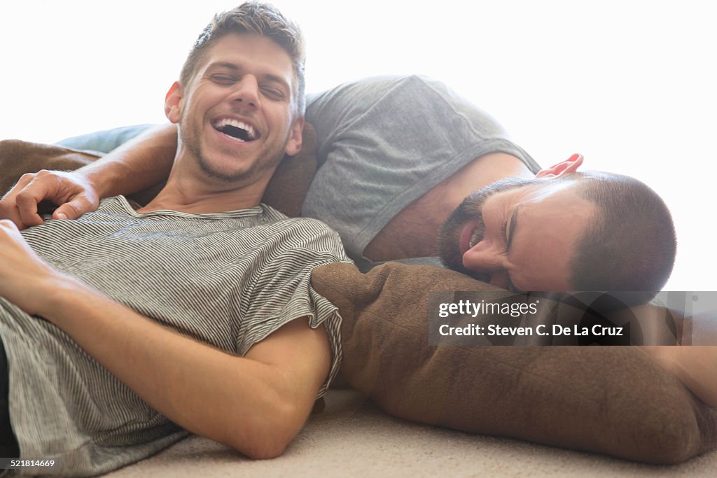 Male couple reclining and laughing on sitting room floor cushions