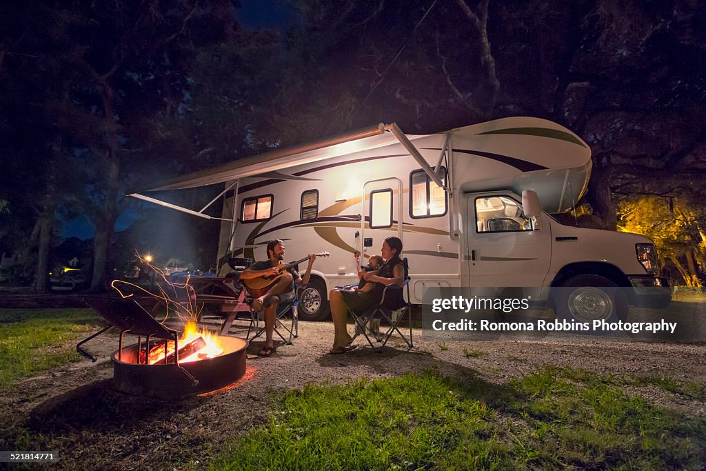 Mid adult couple and baby daughter sitting in front of campfire at night