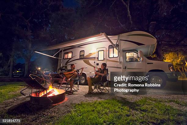 mid adult couple and baby daughter sitting in front of campfire at night - motor home foto e immagini stock
