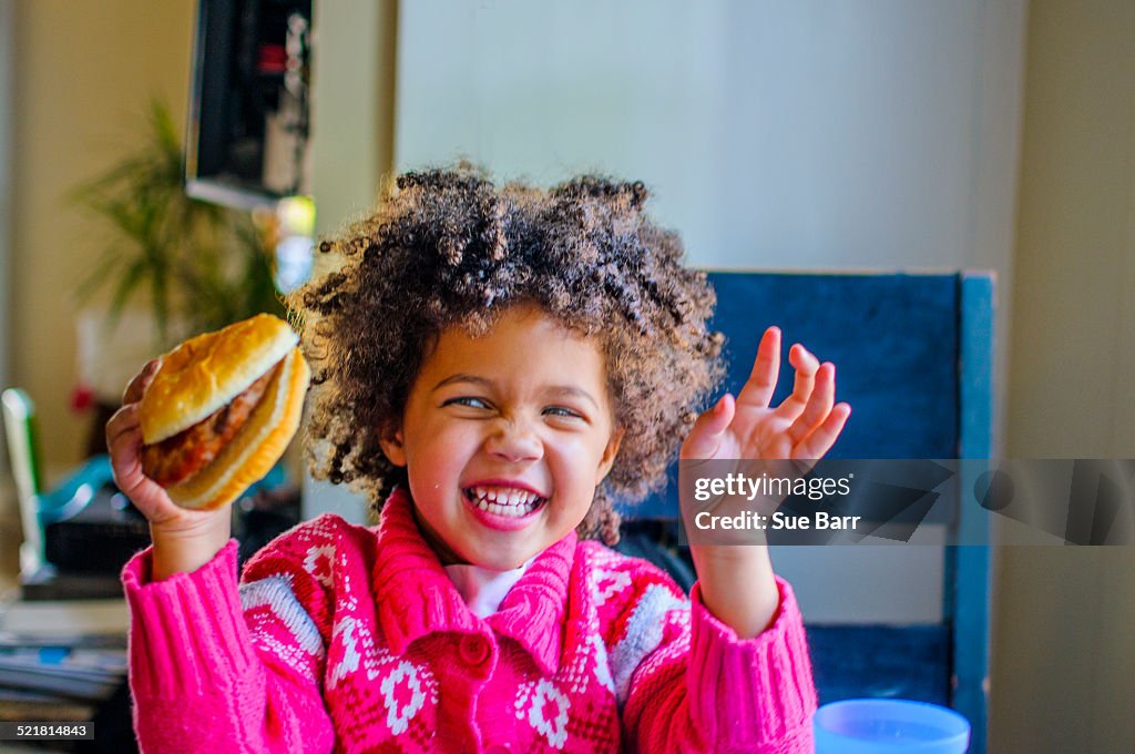 Cute girl laughing and holding up hamburger in kitchen