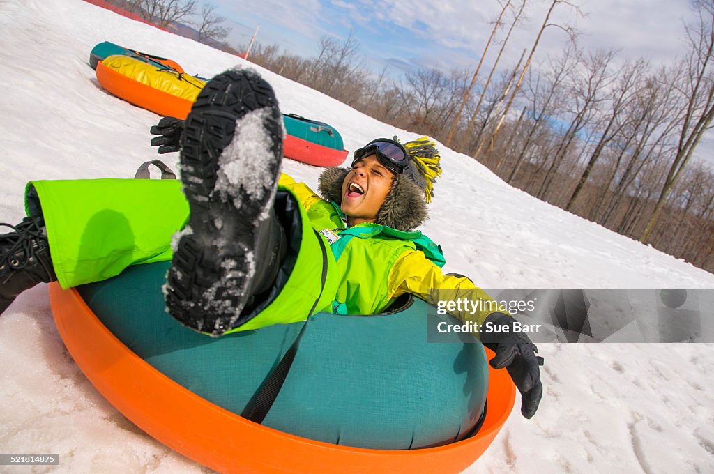 Boy laughing whilst tobogganing down snowy hill