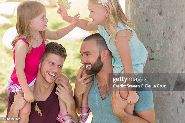 two sisters sitting on fathers shoulders in park - front view portrait of four children sitting on rock stock-fotos und bilder