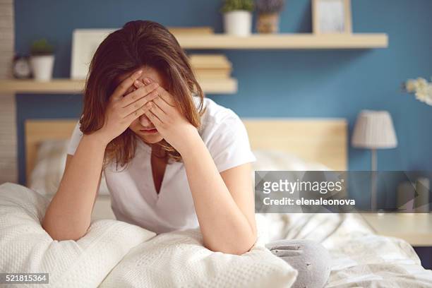 unhappy girl in a bedroom - hoofdpijn vrouw stockfoto's en -beelden
