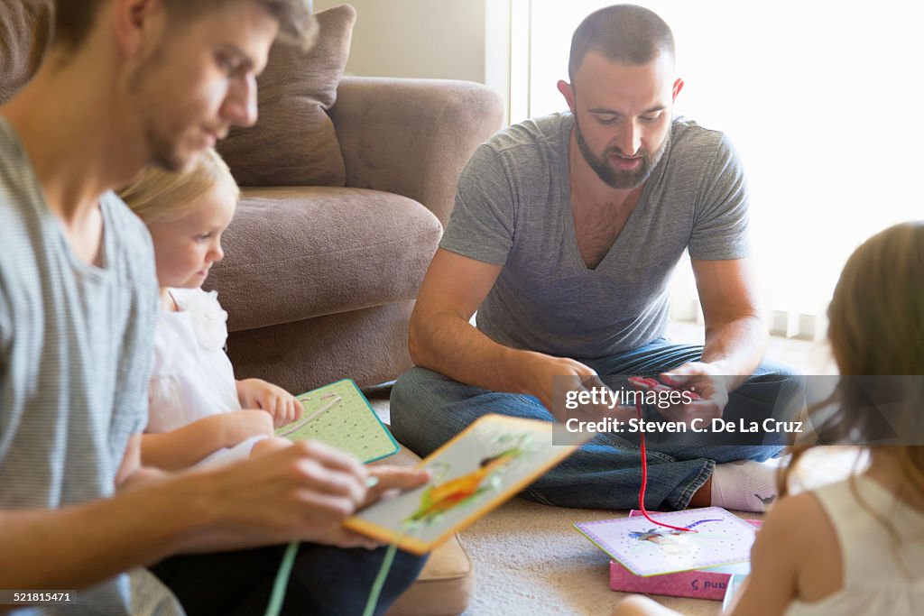 Male couple and two daughters threading picture books on sitting room floor
