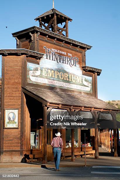 Man in western gear walks past restored historic emporium on Main Street of the Old West town of Winthrop in Washington State