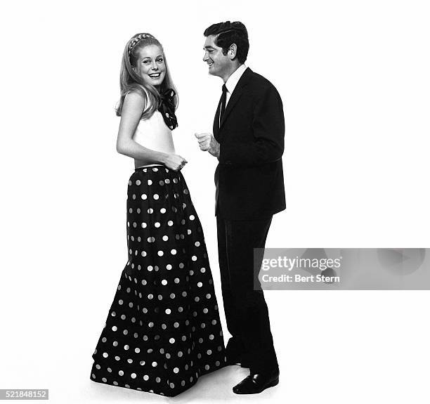 Catherine Deneuve, actress, wearing black taffeta dress with white coin-dot skirt and white halter top, with director Jacques Demy.