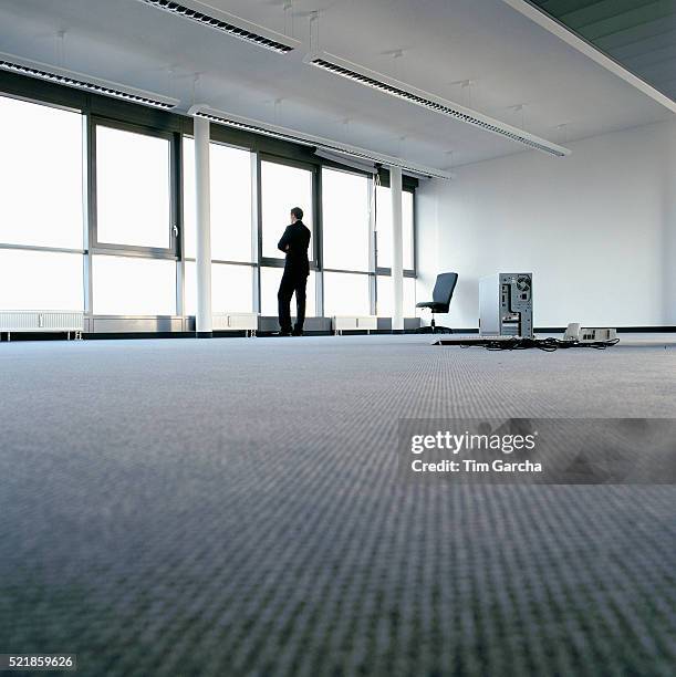 businessman standing in empty office looking out of window - falência imagens e fotografias de stock