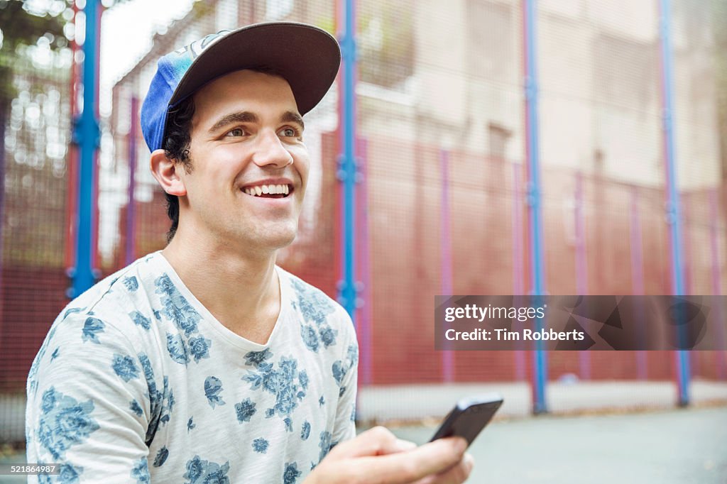 Young man with smart phone at basket ball court.