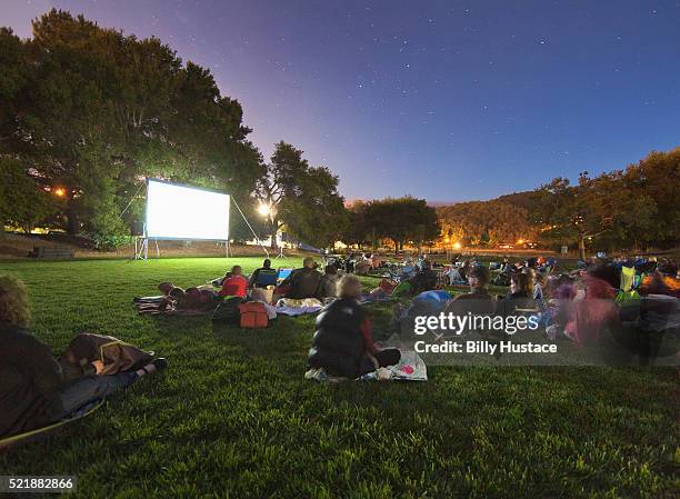 people sitting in a park in front of an illuminated projection screen - public park at night stock pictures, royalty-free photos & images