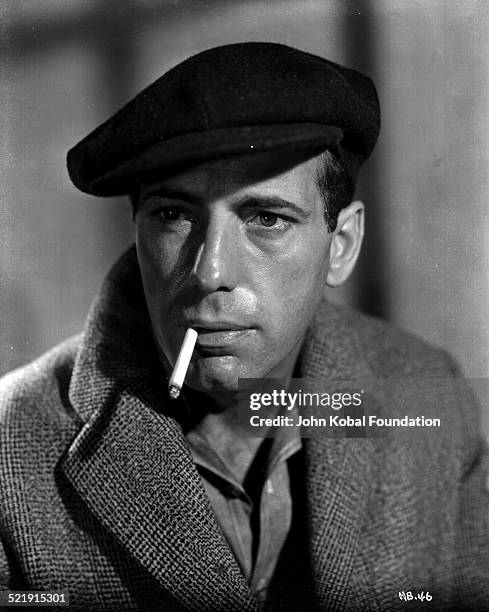 Headshot of actor Humphrey Bogart , wearing a flat cap and smoking a cigarette, as he appears in the movie 'San Quentin' for Warner Bros Studios,...