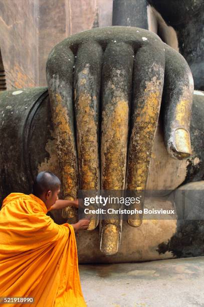 monk applying gold offering to buddha's hand - wat si chum stockfoto's en -beelden