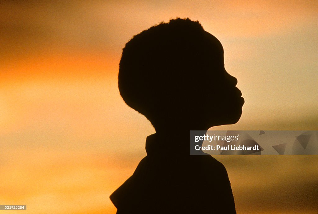 A silhouette of a young West African girl at sunset