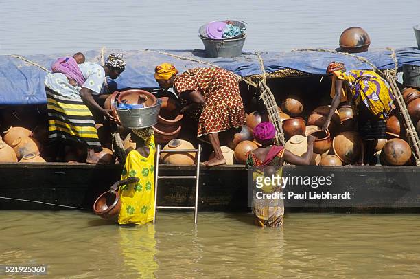 women unload pottery from a piroque in the niger river - niger river stock pictures, royalty-free photos & images