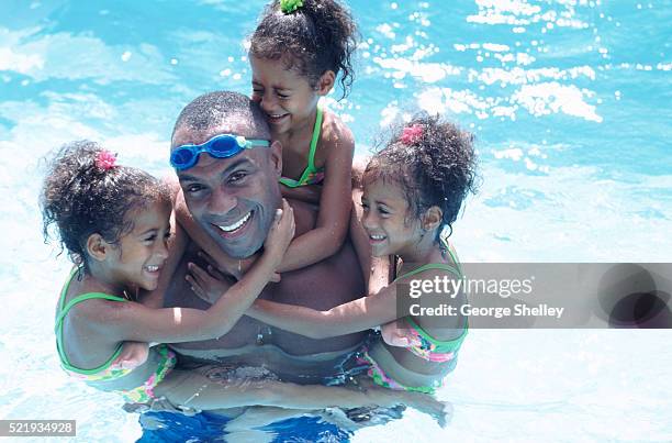 father playing with triplet daughters in pool - triplet girls stock pictures, royalty-free photos & images