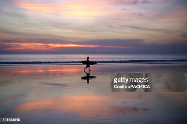 surfer on beach at sunset - kuta stock pictures, royalty-free photos & images