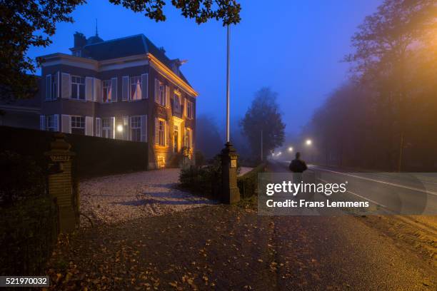 netherlands, man walks near rural estate, twilight - creepy house at night stock-fotos und bilder