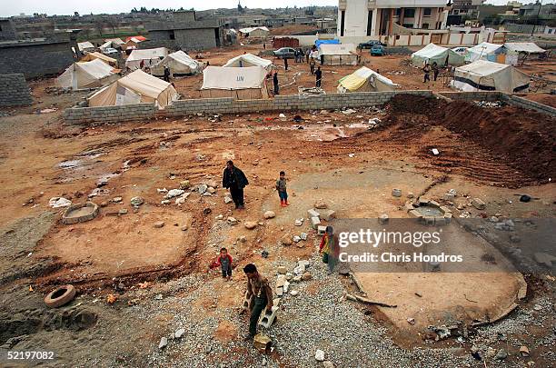 Laborer carries cinderblocks for house while tents for Kurds waiting for homes sit in the background February 13, 2005 in Kirkuk, Iraq. Home building...