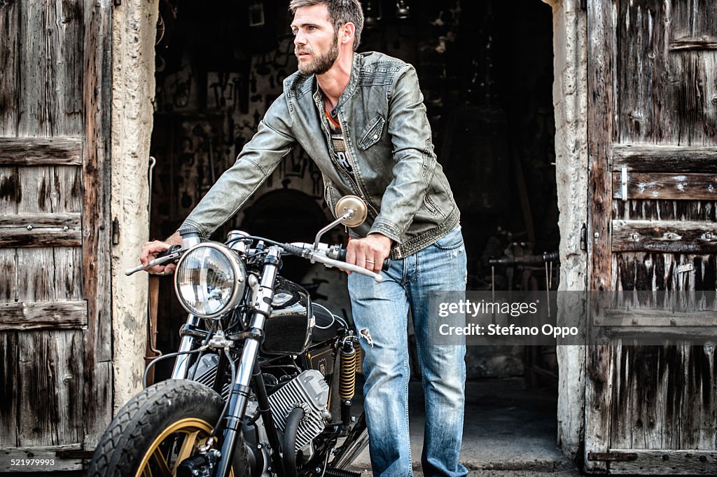 Mid adult man pushing motorcycle out of barn