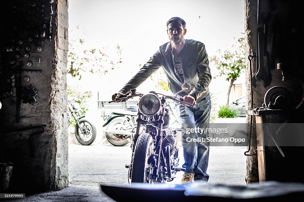 Mid adult man pushing motorcycle through barn doorway