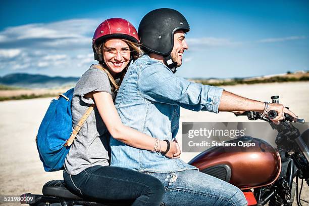 mid adult couple riding motorcycle on arid plain, cagliari, sardinia, italy - motorradfahrer stock-fotos und bilder