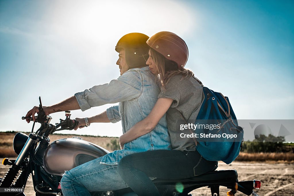 Mid adult couple motorcycling on arid plain, Cagliari, Sardinia, Italy