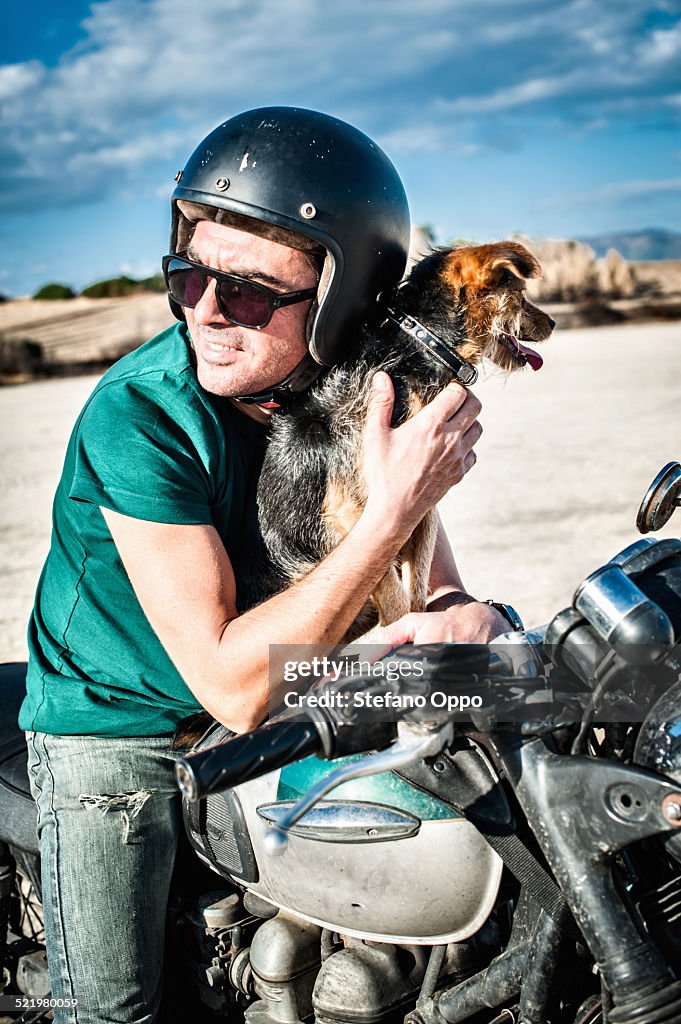 Mid adult man and dog sitting on motorcycle on arid plain, Cagliari, Sardinia, Italy
