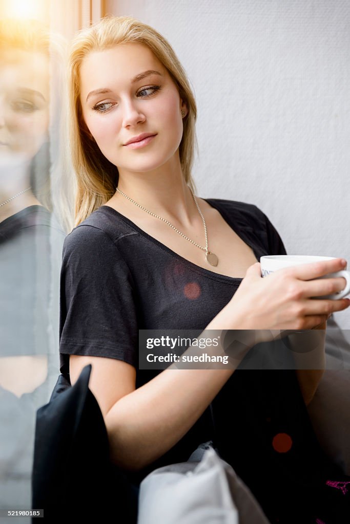 Young woman drinking coffee whilst looking out of window