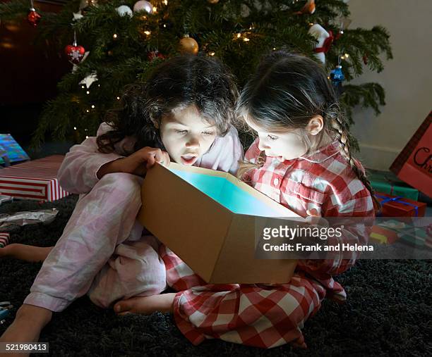 two sisters open mouthed on unwrapping glowing christmas gift box - girl open mouth stockfoto's en -beelden