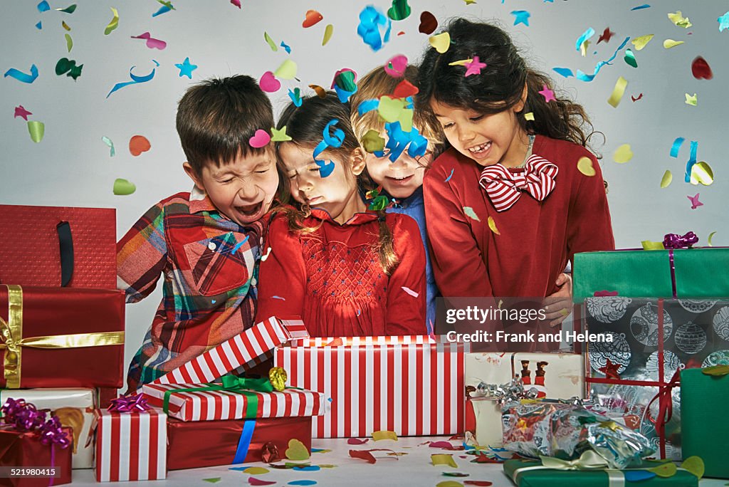 Surprised brothers and sisters unwrapping glowing christmas gift box with exploding confetti
