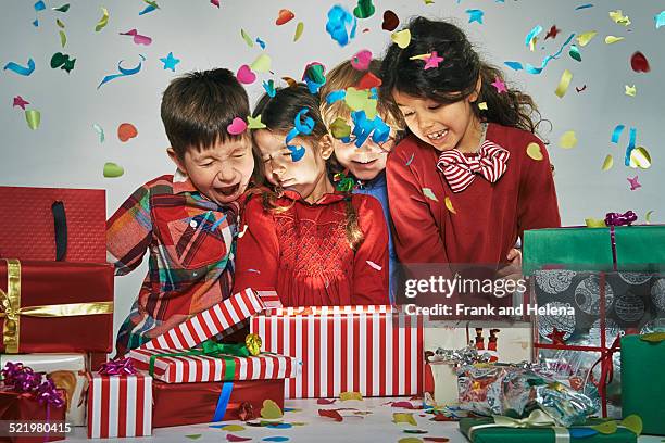 surprised brothers and sisters unwrapping glowing christmas gift box with exploding confetti - exploding box stock pictures, royalty-free photos & images