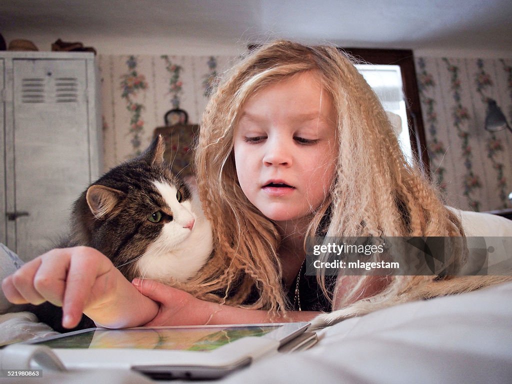 Girl lying on bed with her cat using digital tablet