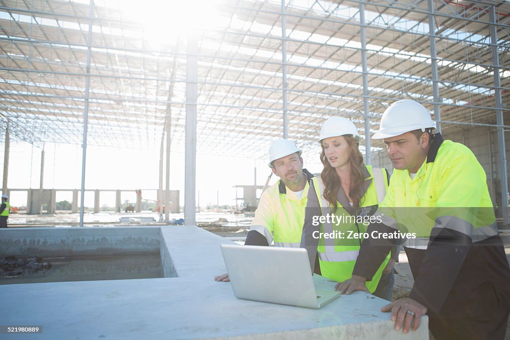 Site managers and architect looking at laptop on construction site