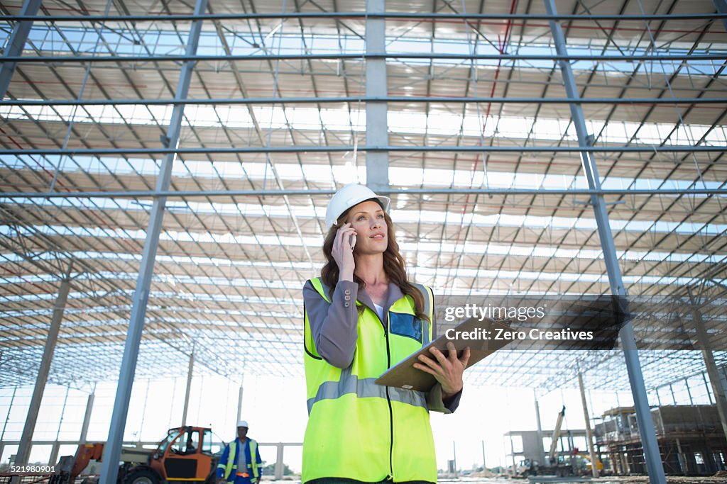 Site manager with clipboard chatting on smartphone on construction site