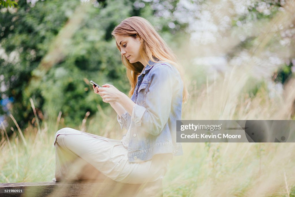 Young woman reading texts on smartphone on park bench