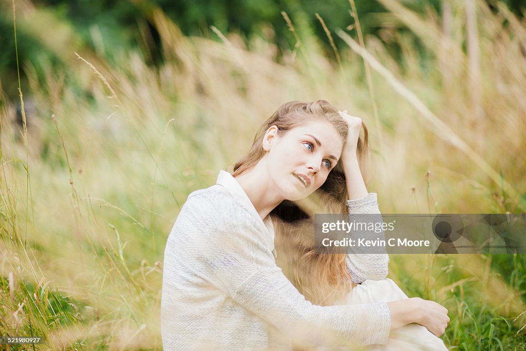 Young woman sitting in long grass with hand in hair