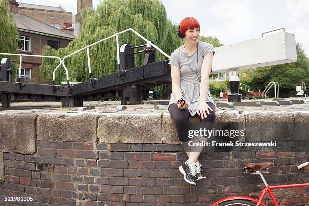 woman listening to music by canal, east london, uk - east london fotografías e imágenes de stock