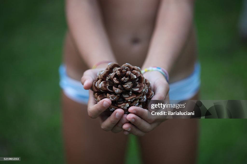 Girl in a bikini holding a pine cone