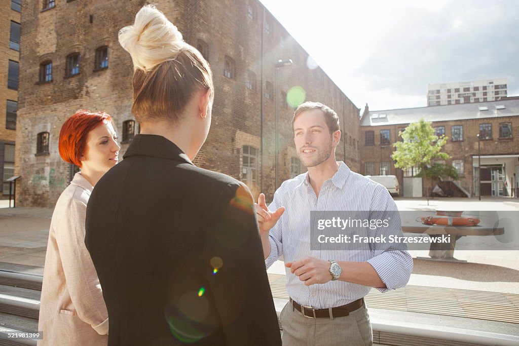 Three young people talking, building in background, East London, UK